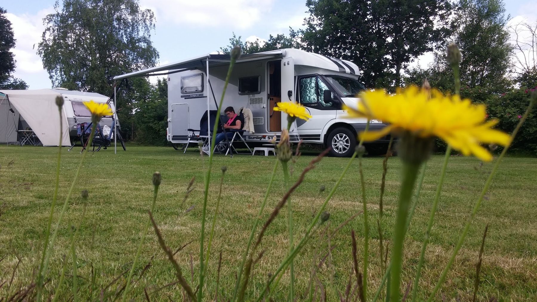 Een camper met uitgedraaide luifel op het veld, met een gele bloem op de voorgrond